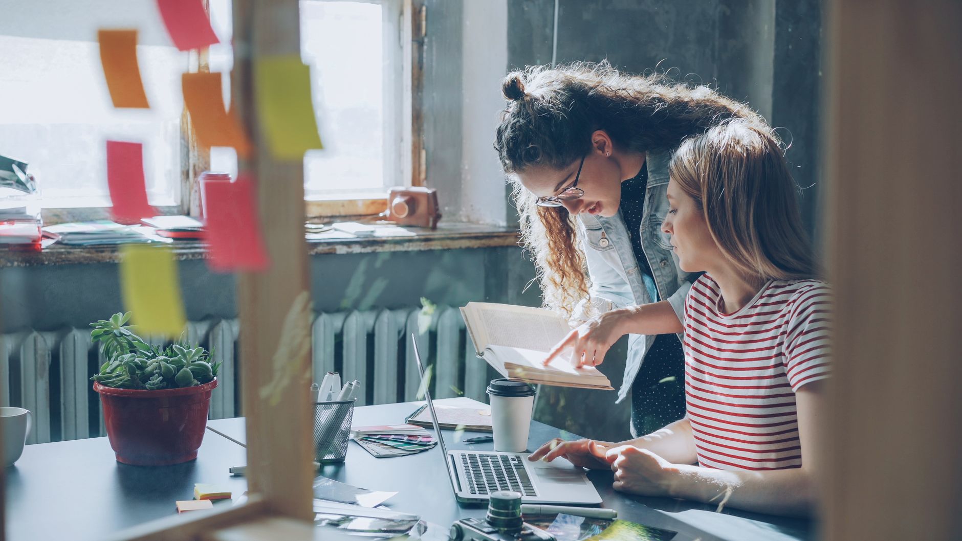 Two women collaborating in a cozy office space with laptops and notes.